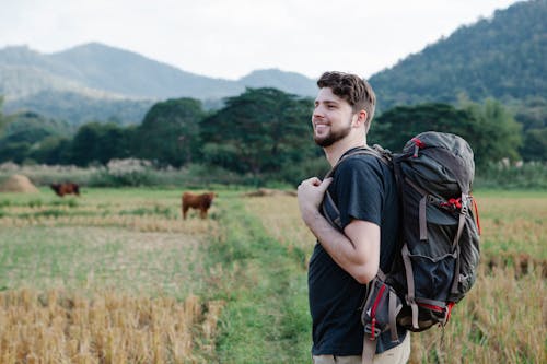 Smiling backpacker admiring nature in field against mountains