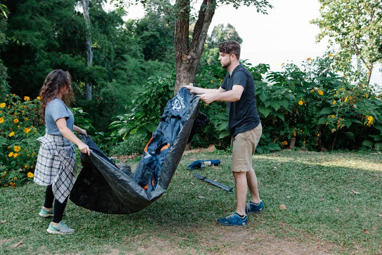 Couple Of Travelers Setting Up Tent On Lawn In Summer