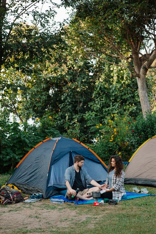 Free Full body of young romantic couple in casual clothes recreating near camping tents and communicating after hiking trip in green forest on sunny day Stock Photo