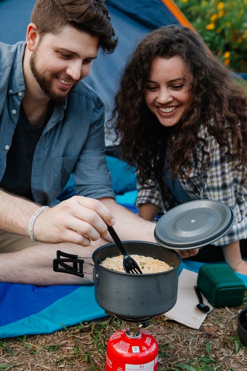 Free Delighted young couple smiling while stirring food in saucepan placed on portable gas stove during lunch preparation at campsite in forest Stock Photo