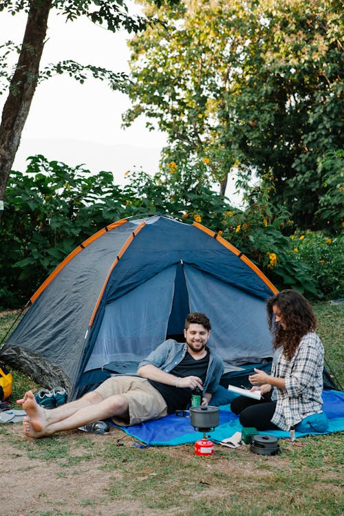 Smiling young couple resting near tent during romantic picnic in woods