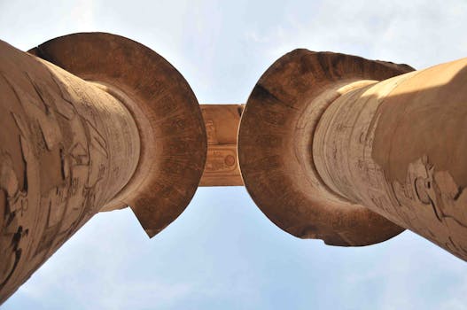 Low angle view of ancient Egyptian columns with hieroglyphs against a blue sky.