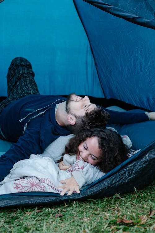 Cheerful young male traveler smiling and lying on happy girlfriend while having fun together in camping tent