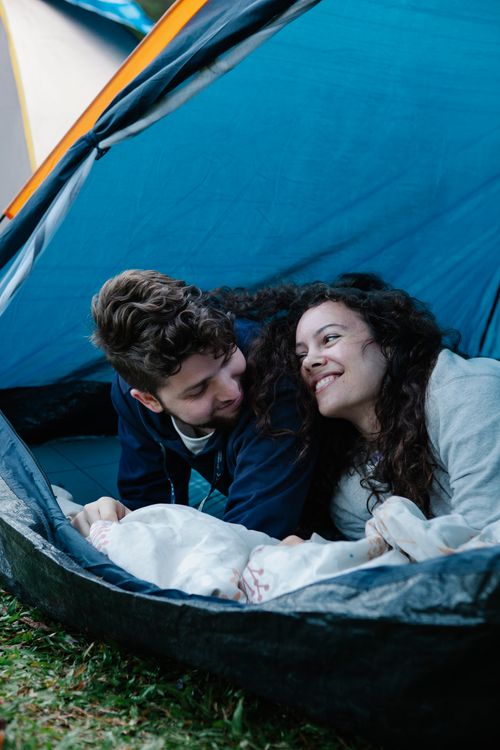 Free Happy loving young couple in warm clothes smiling and looking at each other while recreating in tent during camping Stock Photo