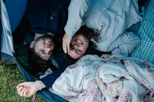 Free Top view of young happy couple in casual clothes smiling and lying in tent during romantic picnic in park Stock Photo