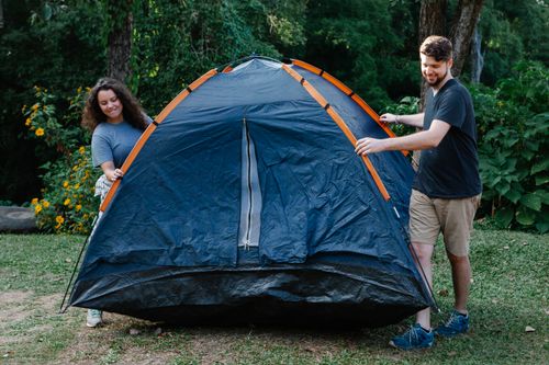 Free Happy couple of travelers in casual clothes pitching tent on green grass in forest during hike in daytime Stock Photo