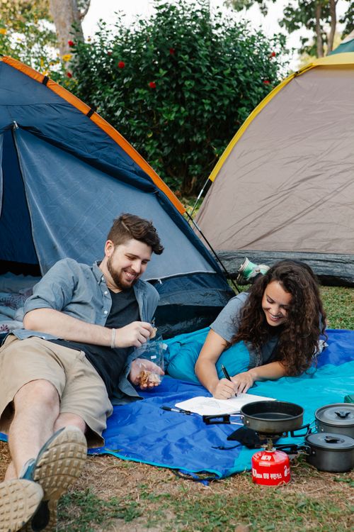 Free Couple of travelers lying on ground near tents among green plants during hike trip in nature in daytime Stock Photo