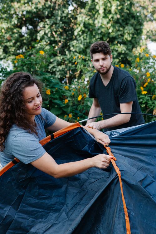 Free Calm couple of travelers setting tent together among green plants in forest during hike trip in daytime Stock Photo