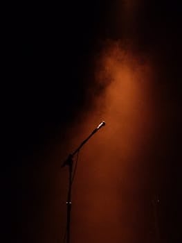 A microphone stands ready on a dimly lit stage, enveloped in atmospheric smoke.