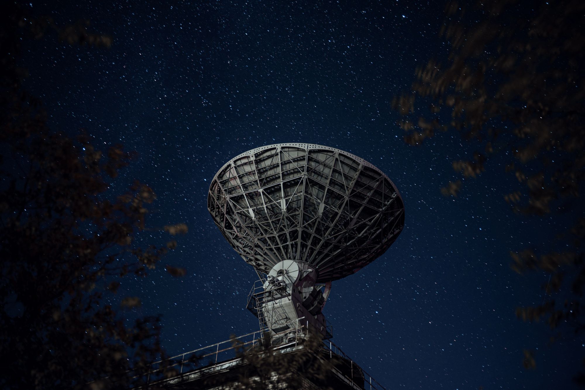 Antena de un radiotelescopio apuntando al cielo nocturno estrellado
