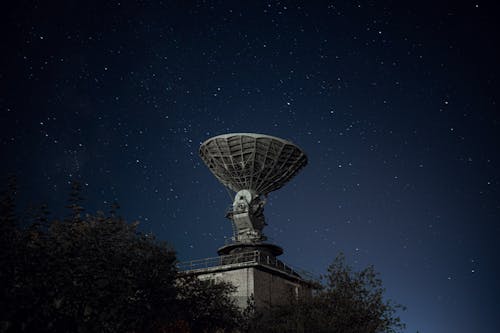 Free Radio telescope and green lush trees under blue sky with stars at night Stock Photo