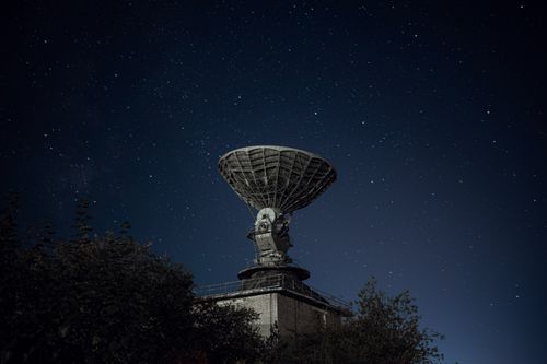 Free Radio telescope and green lush trees under blue sky with stars at night Stock Photo