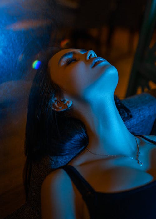 Young dreamy female laying on sofa while resting with closed eyes under bright illumination
