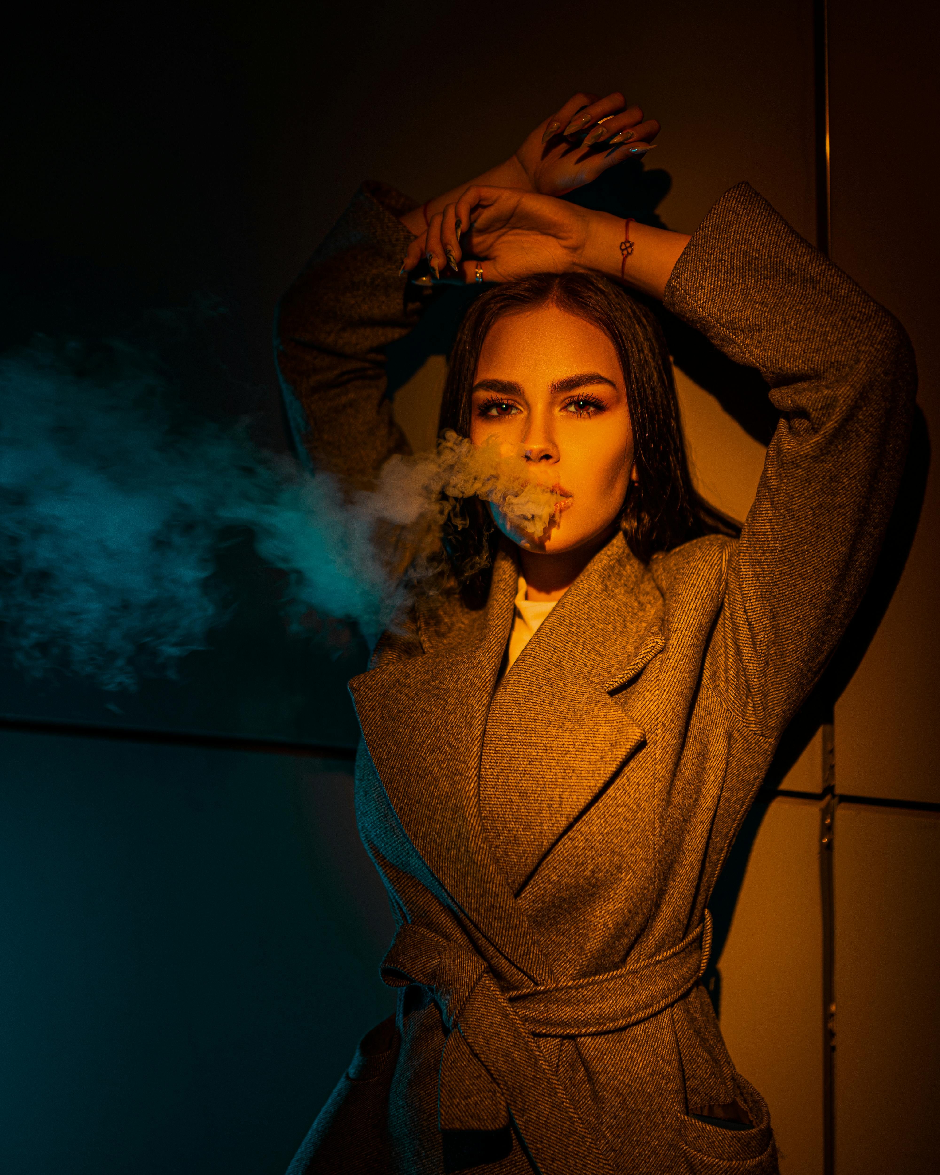 stylish woman exhaling smoke in light