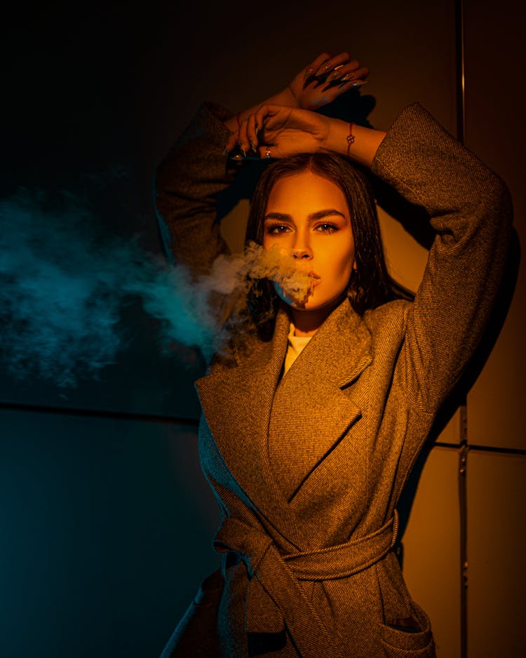 Stylish Woman Exhaling Smoke In Light