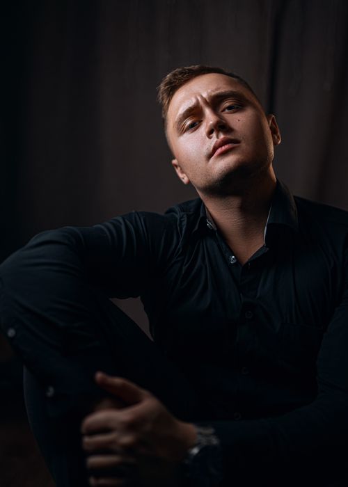 Free Serious male in stylish outfit sitting with hands on knee and looking at camera Stock Photo