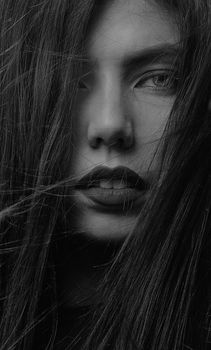 Close-up black and white portrait of a woman with expressive features and messy hair.