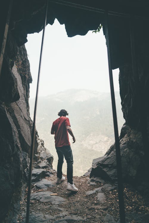 Free Man in Red Shirt and Black Pants Standing Near the Cave  Stock Photo