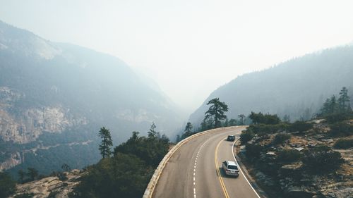 Free Curved mountain road with cars driving through a foggy landscape and forested hills. Stock Photo