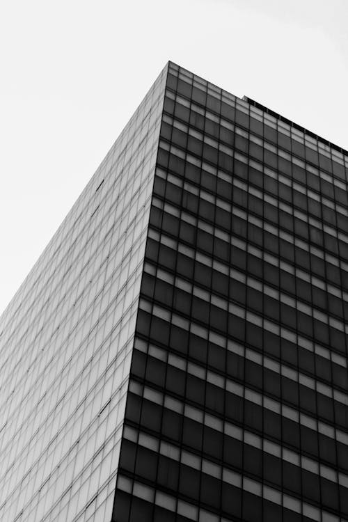 From below of black and white corner of modern multistory building with symmetric windows against cloudy sky