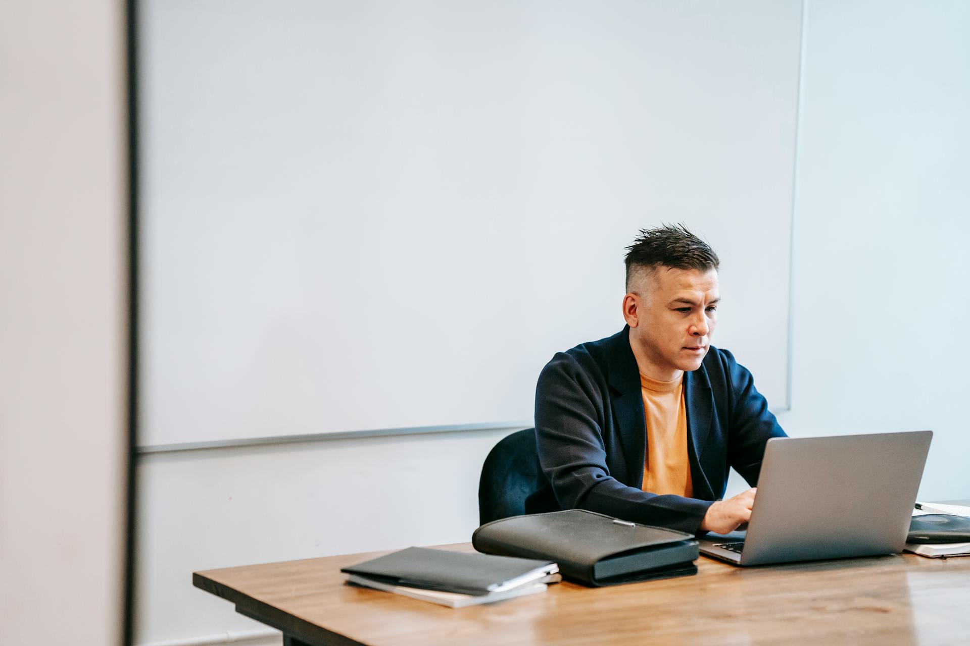 Focused businessman typing on laptop at office desk with whiteboard.