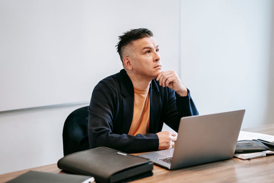 Thoughtful man working on a laptop in an office setting, engaged in remote work.