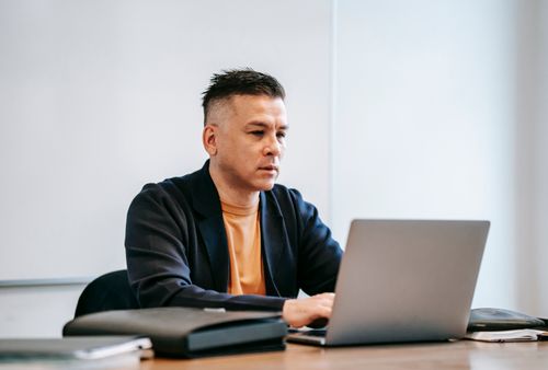 Free A concentrated man working remotely on his laptop in a modern indoor office setting. Stock Photo