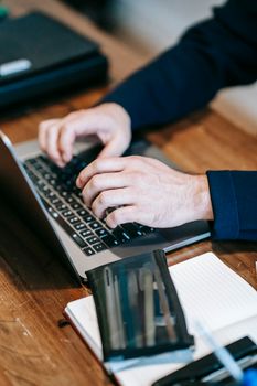 Close-up of hands typing on a laptop with a notebook on a wooden desk, ideal for remote work themes.