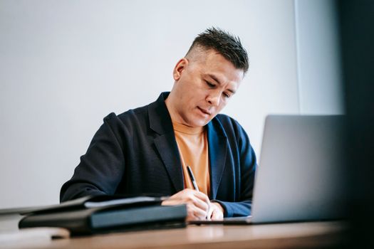 Man engaged in work, writing notes at a desk with a laptop.