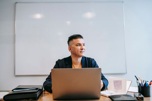 Free A man engaged in remote work, focused in a home office setting with a laptop and whiteboard. Stock Photo