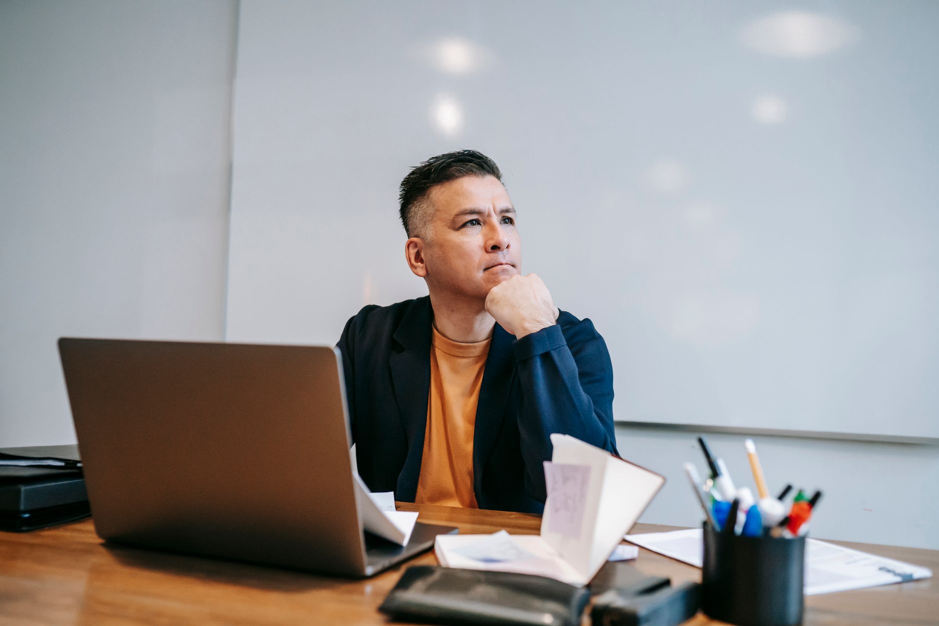A thoughtful man works remotely in a home office setting, surrounded by digital devices and notes.
