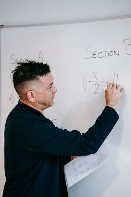 A male teacher explaining a math problem on the whiteboard with a marker. A male teacher explaining a math problem on the whiteboard with a marker.