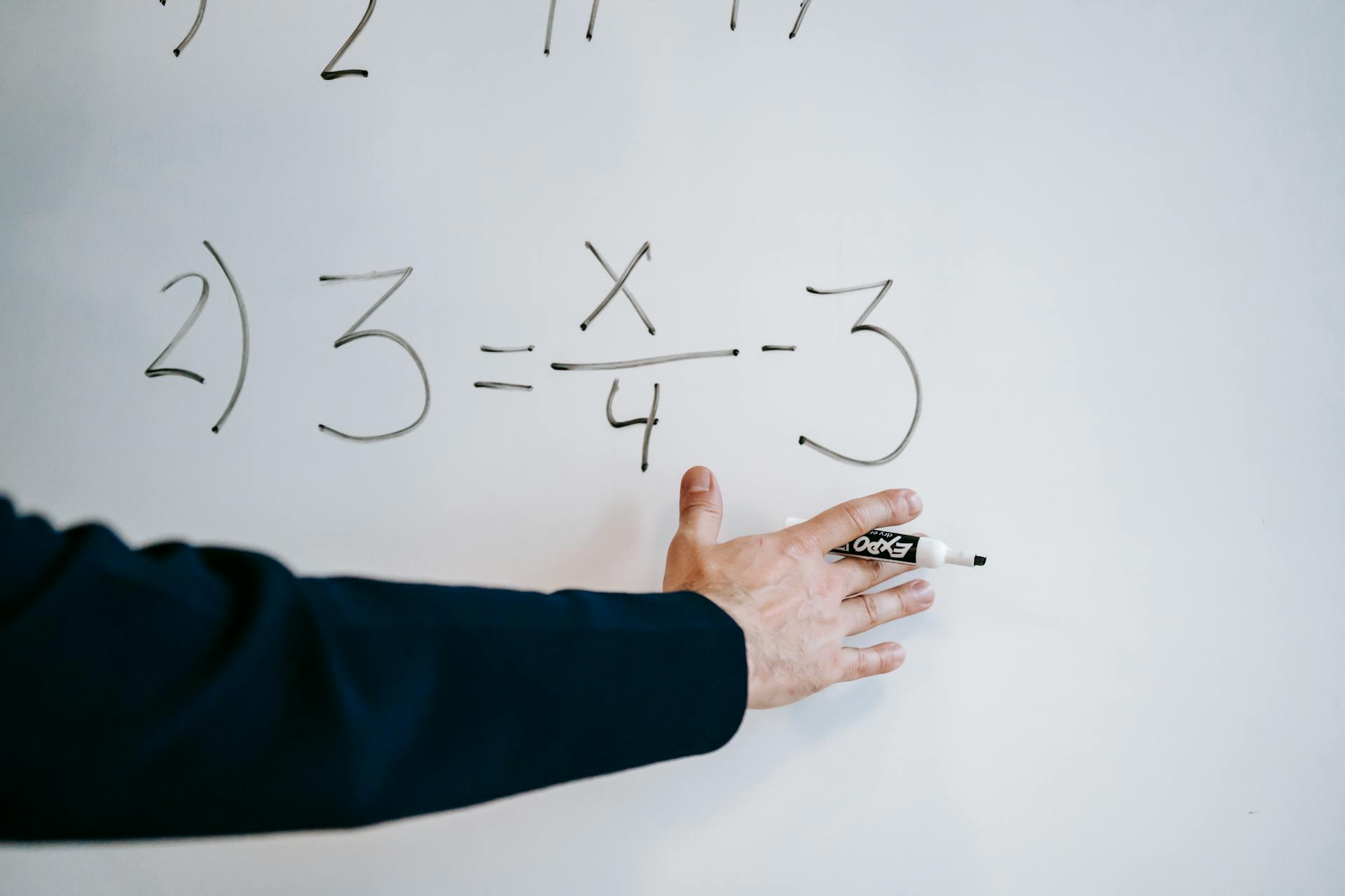 A hand writing a mathematical equation on a whiteboard with a marker.