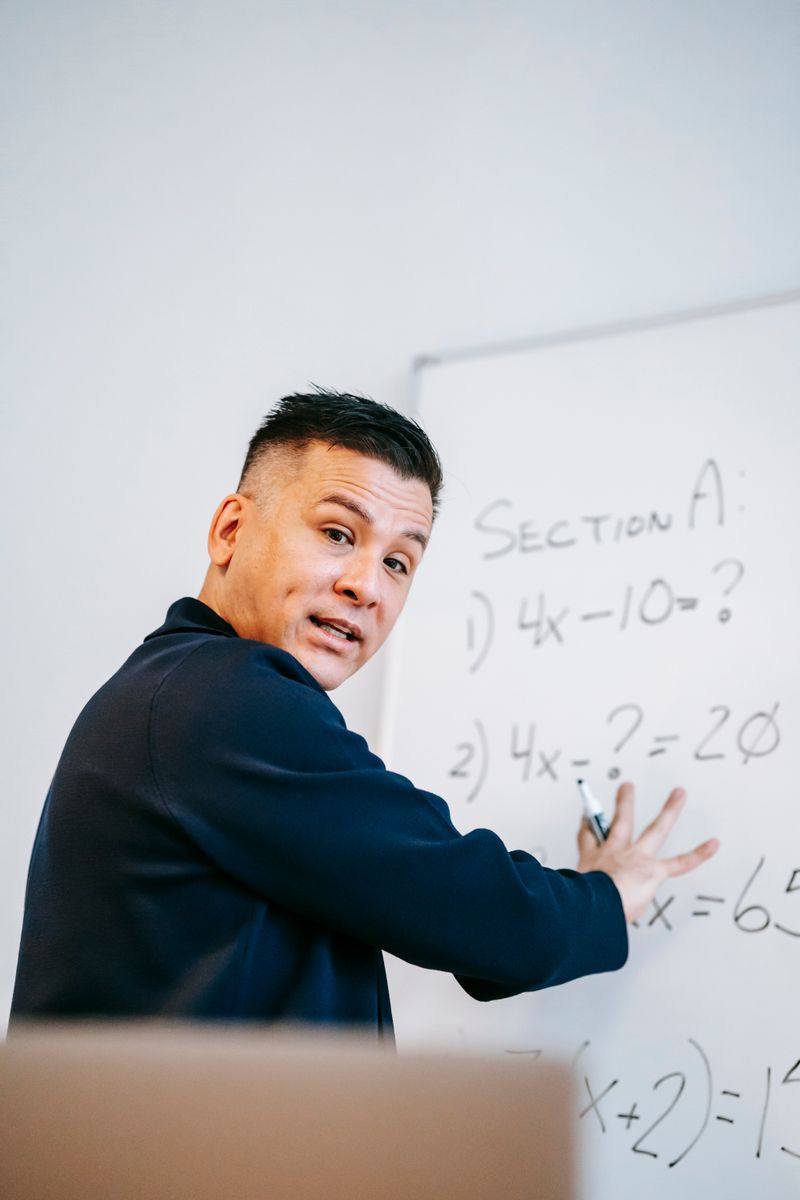 Math instructor solving equations on whiteboard during lesson.