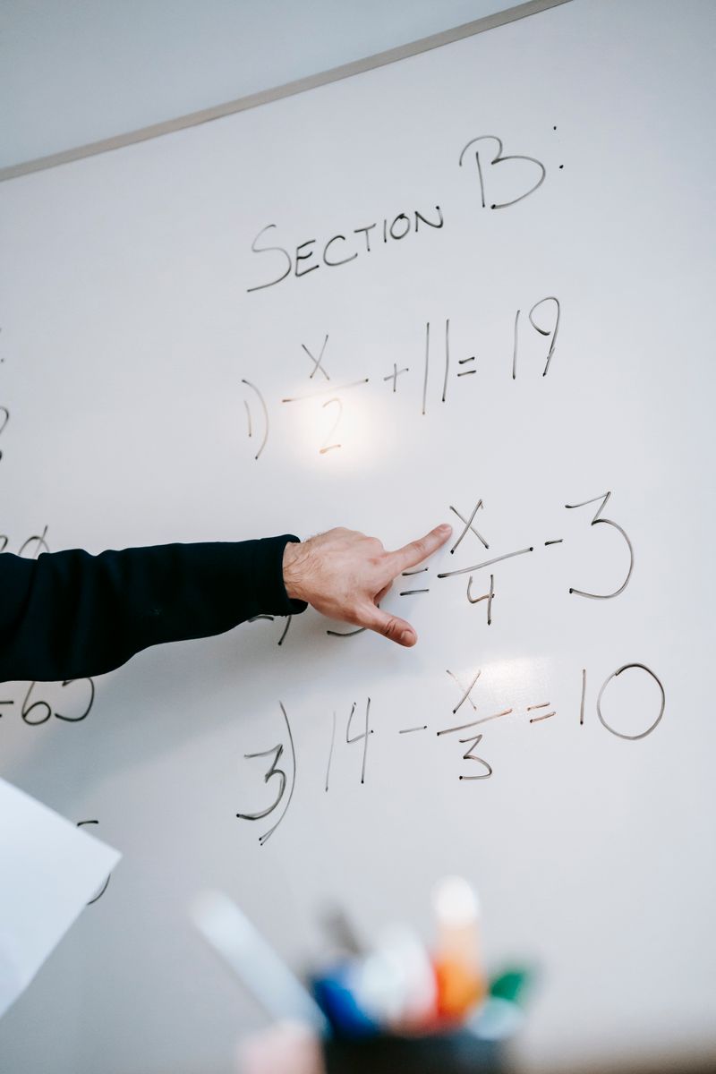 Close-up of an instructor's hand solving math equations on a whiteboard during a lesson.