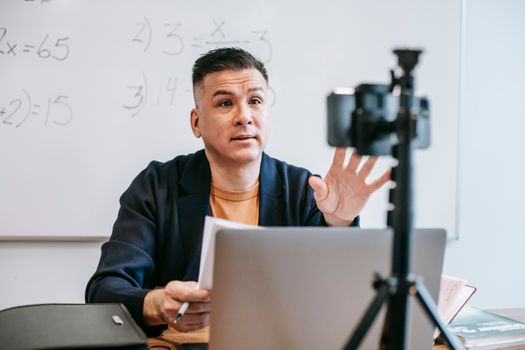 A male instructor conducting an online teaching session using a laptop and camera setup.