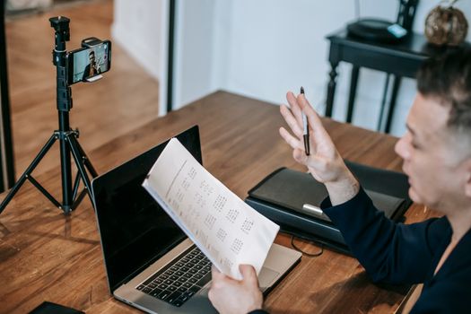 A man conducting an online teaching session using a laptop and smartphone on a tripod.