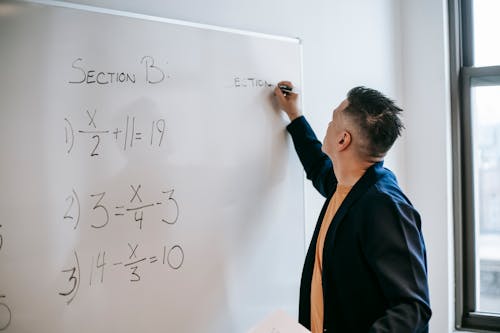 Focused worker writing equations on whiteboard in office in daytime