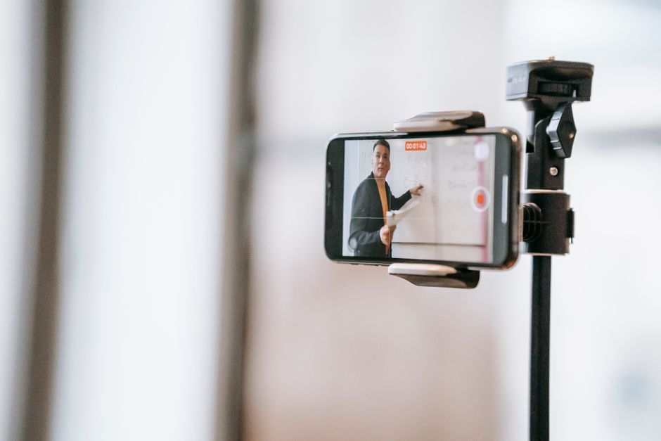 Um professor conduzindo uma aula online usando um smartphone montado em um tripé.