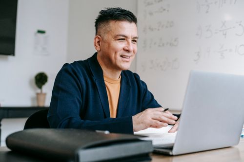 Free Smiling professional man engaged in remote work using a laptop in a modern office setting. Stock Photo