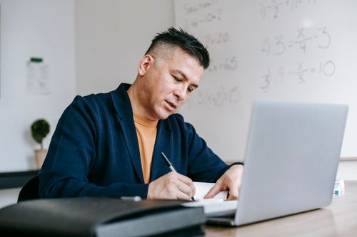 Free Focused professional writing notes at home office desk with laptop. Stock Photo
