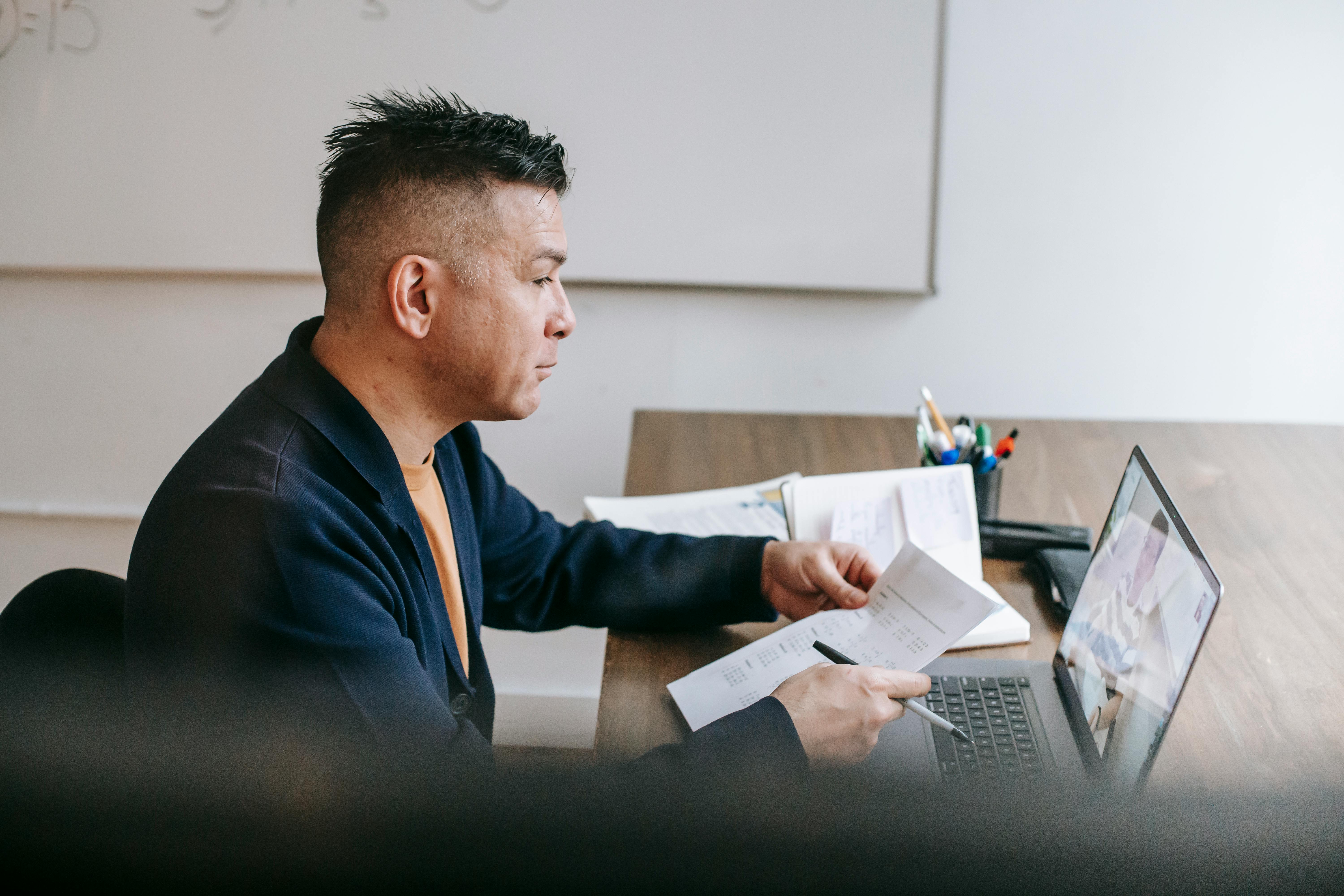 man video chatting on laptop with coworker near documents