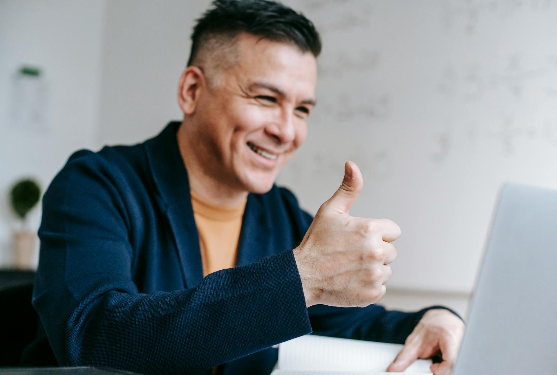 Smiling man giving thumbs up while working on laptop from home office, illustrating positive remote work experience.