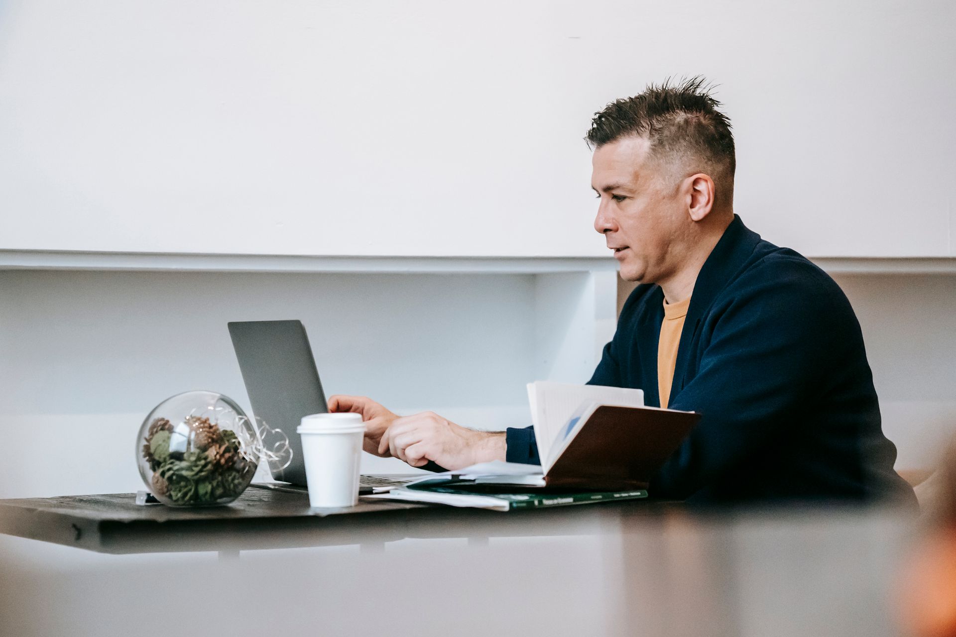 An adult man engaged in remote work on a laptop with coffee in a cozy home office setting.