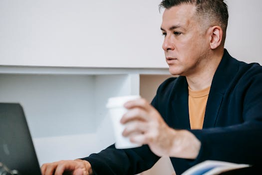 Adult man working on a laptop with coffee indoors, depicting remote work lifestyle.