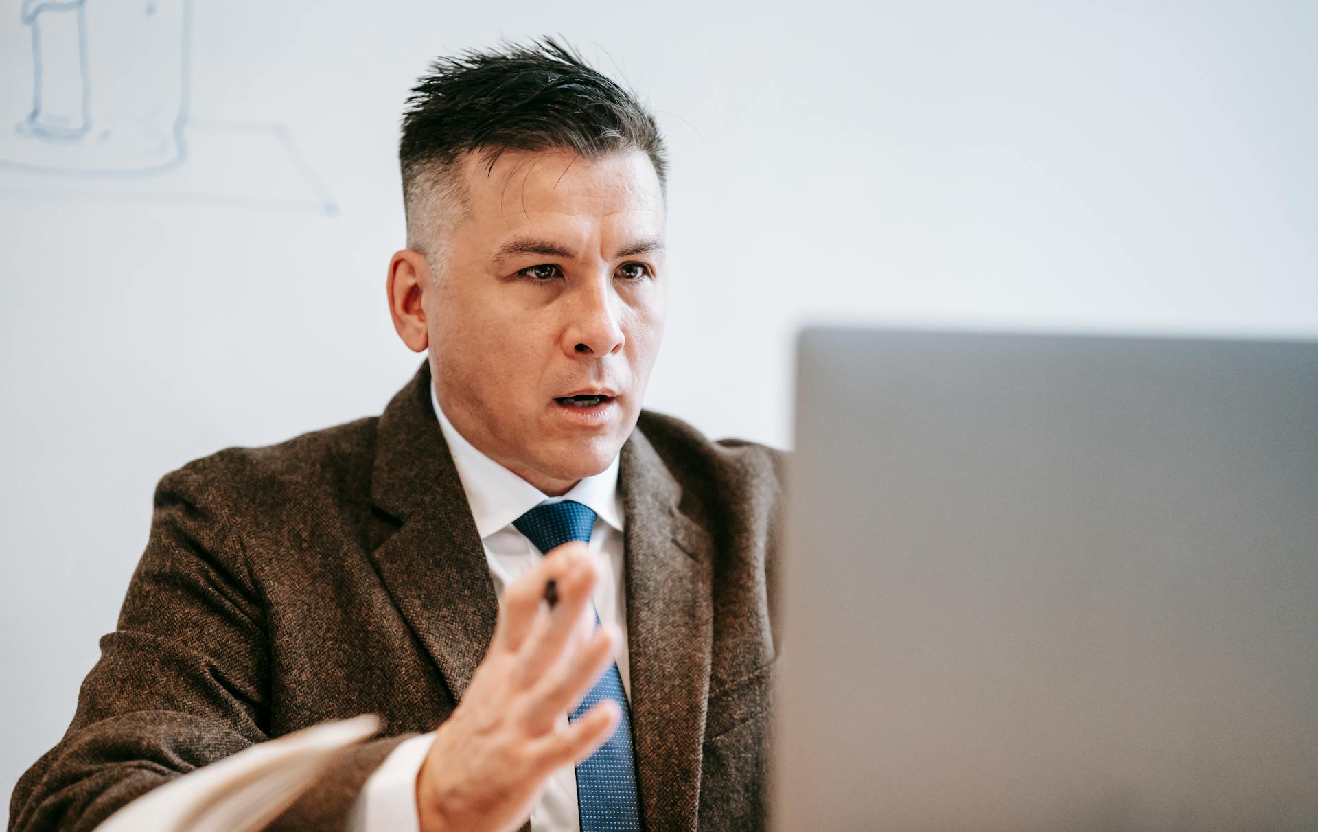 Professional businessman in formal attire engaged in an online meeting using a laptop.