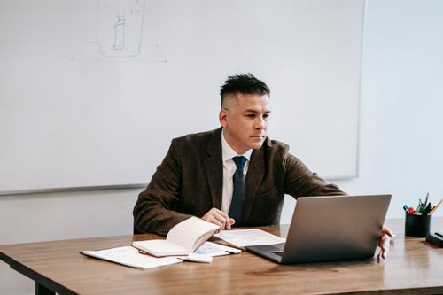 Free Man in suit working on laptop with papers in modern office setting. Stock Photo