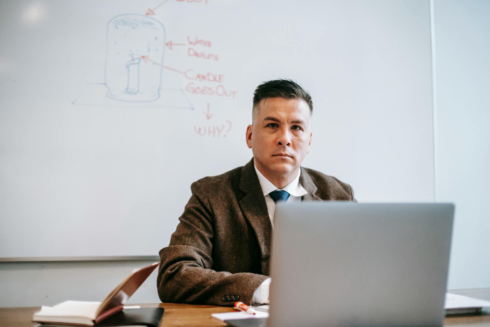 A focused man in formal attire using a laptop in an office setting with a whiteboard.