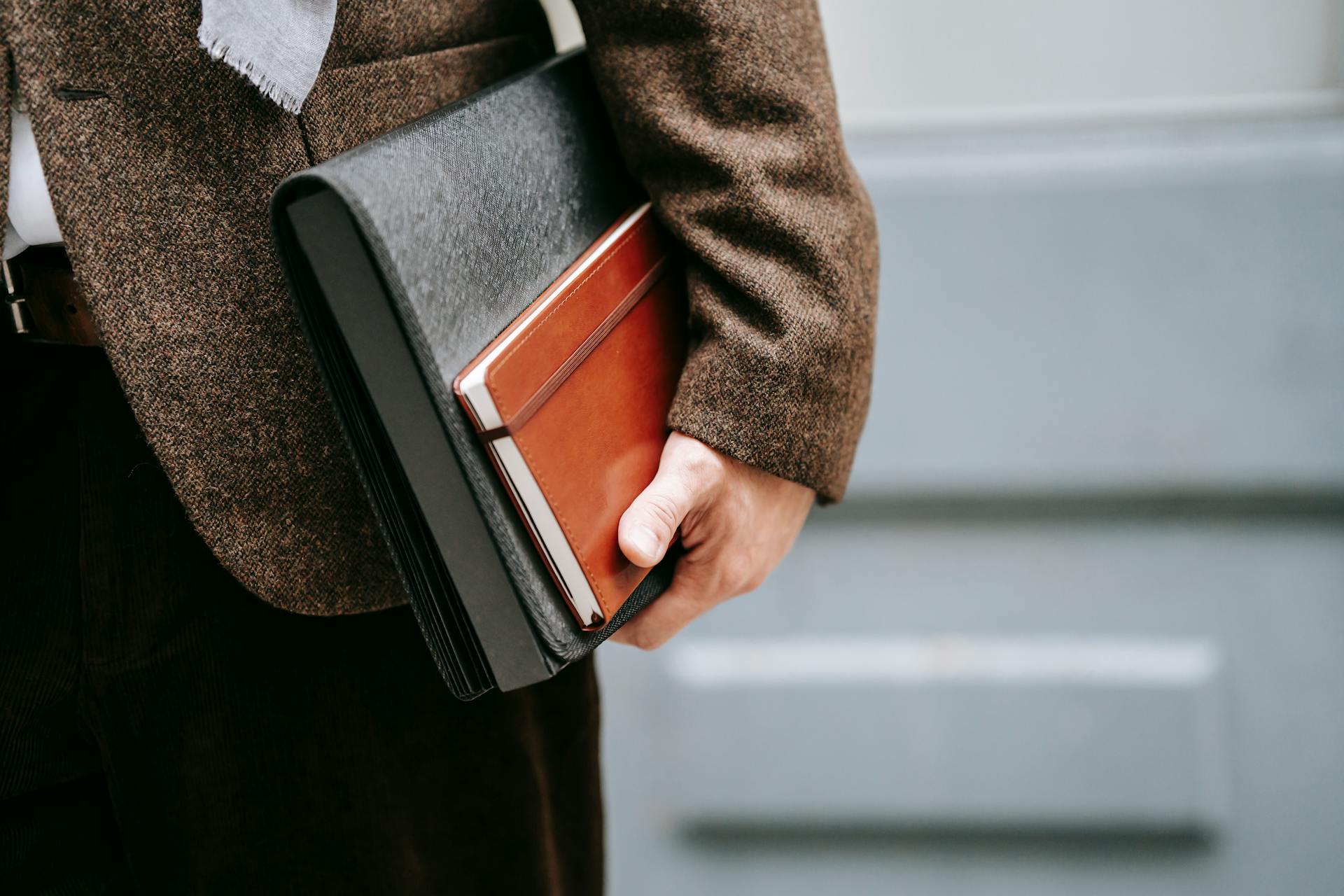 Close-up of an adult holding a brown notebook and portfolio in formal attire.