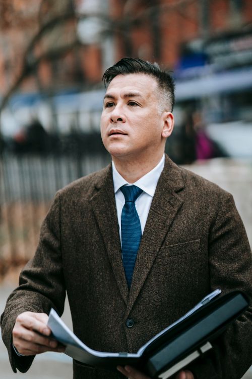 Free Businessman in formal wear looking away while holding a notepad outdoors. Stock Photo